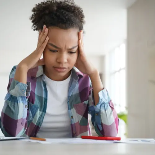 Woman with pen and paper. She is holding her head in frustration