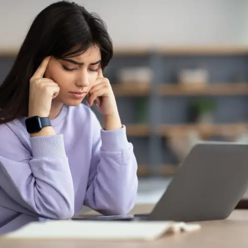 A woman is setting in front of her laptop. She looks frustrated.